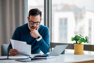 Ein Mann sitzt arbeitend vor seinem Computer und liest Dokumente