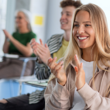 Eine junge Frau sitzt klatschend an einem Tisch.
